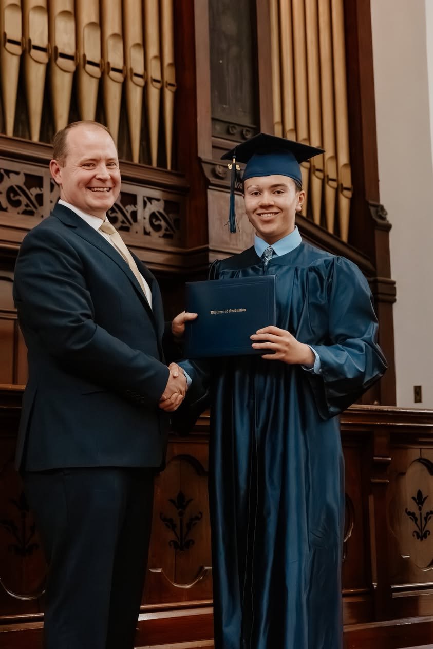 A NECA graduate receiving a diploma and a handshake at commencement.